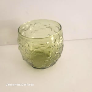 May include: A clear, olive-green glass tumbler with a textured, organic pattern. The glass has a thick base and a rounded shape. The tumbler is likely used for drinking beverages.