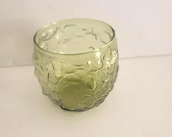 May include: A clear, olive-green glass tumbler with a textured, organic pattern. The glass has a thick base and a rounded shape. The tumbler is likely used for drinking beverages.