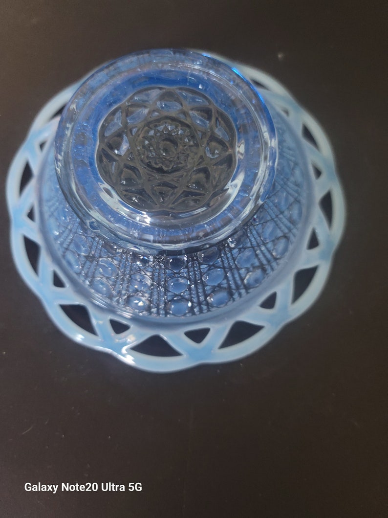 May include: A vintage blue glass bowl with a decorative openwork rim. The bowl has a detailed pattern on the base and sides. The bowl is made of a light blue glass and is likely from the mid-20th century.