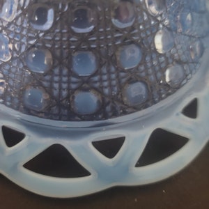 May include: Close-up of a light blue glass bowl with a decorative pattern. The bowl features a lattice design with raised circular accents and a scalloped edge. The glass has a translucent quality, and the bowl sits on a dark surface.