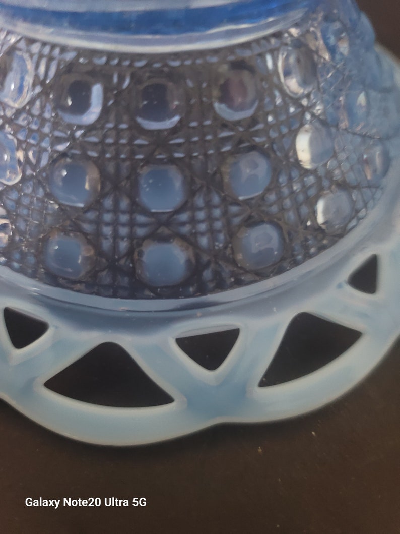 May include: Close-up of a light blue glass bowl with a decorative pattern. The bowl features a lattice design with raised circular accents and a scalloped edge. The glass has a translucent quality, and the bowl sits on a dark surface.