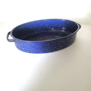 May include: Oval blue enamelware baking dish with white speckles. The dish has two handles and a wide rim. This vintage-style cookware is suitable for baking and serving.