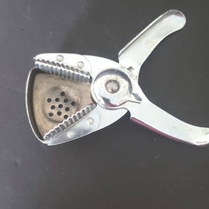 May include: A shiny, silver citrus juicer with a hinged design. The juicer features a perforated bowl for catching juice and a serrated edge for reaming citrus. The handles are curved for easy gripping. The juicer is made of metal.