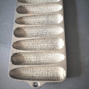 Peut inclure: Moule à pain de maïs en fonte avec sept moules en forme d'épis de maïs. Le moule est rectangulaire avec un trou de poignée à une extrémité. Les moules ont des textures détaillées pour imiter les grains de maïs. Le moule est de couleur gris foncé.