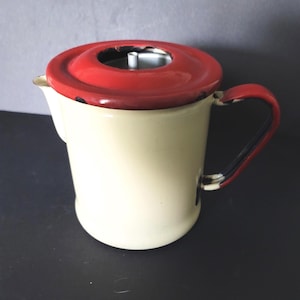 May include: Cream-colored enamelware coffee pot with a red lid and handle. The handle is accented with black and red stripes. The pot has a spout and a lid with a hole in the center. A vintage kitchenware item.