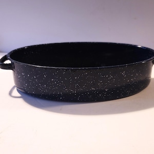 May include: A speckled, dark blue enamel roasting pan with two side handles. The oval-shaped pan has a speckled white pattern throughout the dark blue enamel. This kitchenware is suitable for baking and roasting.