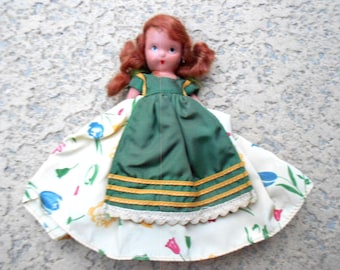 May include: A vintage doll with red hair and blue eyes, wearing a green dress with gold trim and a floral patterned skirt. The doll's dress has a white lace trim. The doll is a classic toy.
