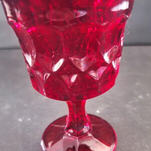 Op de afbeelding: Een robijnrode kelk in vintage-stijl met een textuur van diamantpatroon. De steel en voet zijn effen rood en het glas heeft een lichte glans. Dit decoratieve glas is geschikt voor het serveren van dranken.
