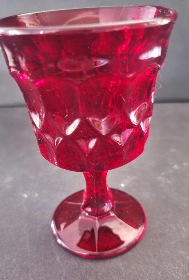 Op de afbeelding: Een robijnrode kelk in vintage-stijl met een textuur van diamantpatroon. De steel en voet zijn effen rood en het glas heeft een lichte glans. Dit decoratieve glas is geschikt voor het serveren van dranken.