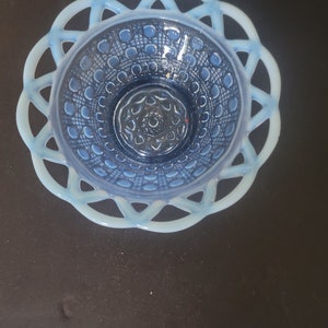 May include: A vintage blue glass bowl with a decorative lattice rim. The bowl features a detailed pattern of circles and lines within the bowl's interior. The rim is a lighter shade of blue, creating a contrast with the darker blue interior.
