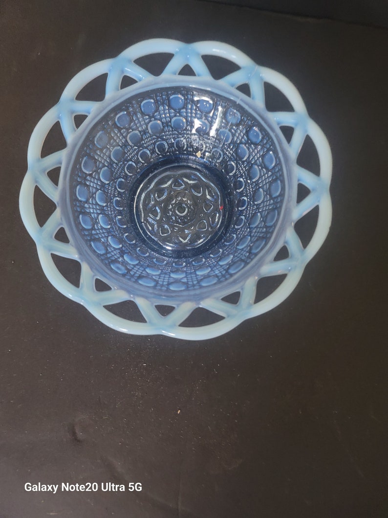 May include: A vintage blue glass bowl with a decorative lattice rim. The bowl features a detailed pattern of circles and lines within the bowl's interior. The rim is a lighter shade of blue, creating a contrast with the darker blue interior.