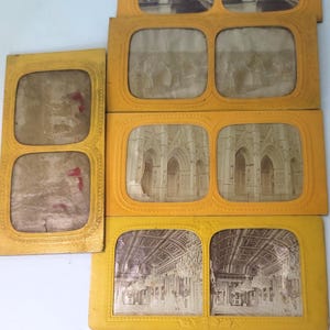 May include: A collection of vintage stereoscopic cards with yellow frames. The cards feature sepia-toned images of bridges, architecture, and interiors. The frames have a decorative border.