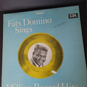 Puede incluir: Portada de &aacute;lbum de vinilo vintage para Fats Domino Sings. La portada del &aacute;lbum es azul claro con el t&iacute;tulo en blanco. Un c&iacute;rculo de color dorado presenta una foto en blanco y negro de Fats Domino. El texto "Million Record Hits" est&aacute; en la parte inferior.