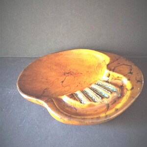 May include: A vintage, oval-shaped ashtray with a brown and gold marbled finish. The ashtray features a built-in rest and a series of grooves for holding cigarettes. The design is simple and functional, suitable for a retro or mid-century modern aesthetic.