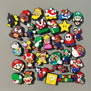 May include: A collection of colorful Super Mario Bros. character charms, including Mario, Luigi, Peach, Bowser, Yoshi, and more. The charms are made of rubber and have a variety of designs. The charms are perfect for adding a touch of fun to your keys, bags, or other accessories.
