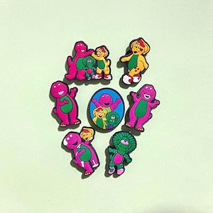 May include: A set of eight purple and green dinosaur figurines. The dinosaurs are all different sizes and poses. Some of the dinosaurs are holding hands or hugging. The dinosaurs are all smiling.