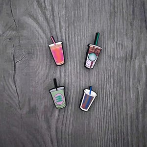 May include: Four different color coffee cup charms with a straw. The charms are green, pink, brown, and blue. The charms are made of silicone and are designed to look like coffee cups.