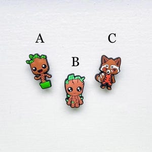 以下が含まれることがあります： カートゥーンキャラクターの靴のチャームが3つ。チャームはゴム製で、緑と茶色のグルート、茶色のグルート、赤と白のロケット・ラクーンが描かれています。