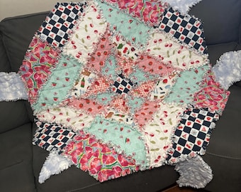 Puede incluir: Una colcha de retazos hecha a mano con un diseño de patchwork que incluye varios patrones de tela como cerezas rojas, rodajas de sandía, fresas y cuadros blancos y negros. La colcha tiene costuras deshilachadas y bordes de tela azul claro texturizada.