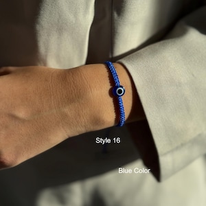 May include: A blue woven bracelet with a central evil eye bead. The bracelet is worn on a wrist, with the text "Style 16" and "Blue Color" visible.