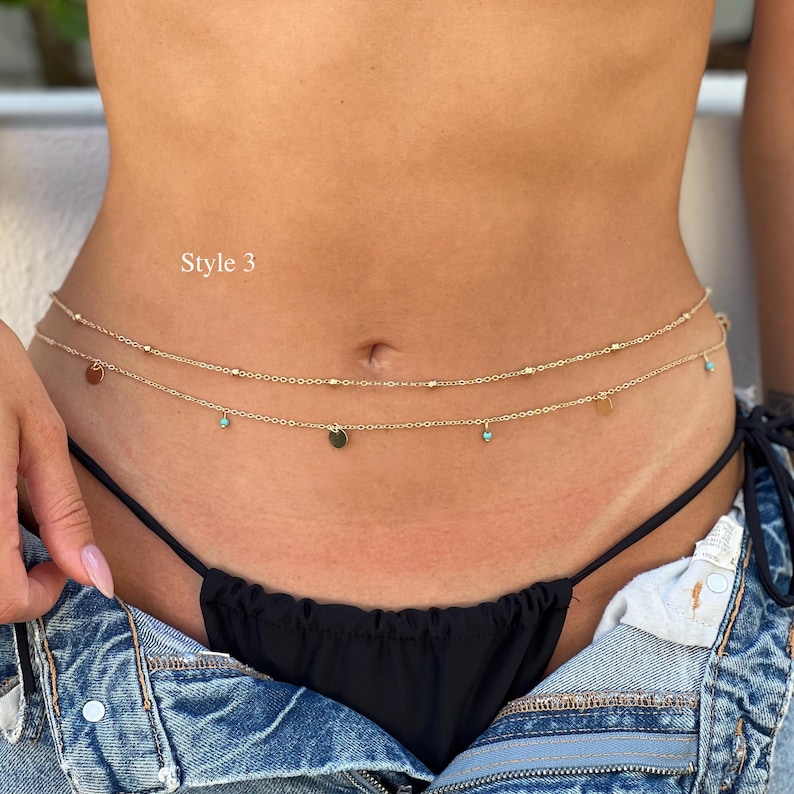 May include: A double-strand gold-toned waist chain featuring small metallic beads and dangling charms, including tiny turquoise-colored accents and flat circular discs. The text "Style 3" is visible on the left side of the jewelry piece.