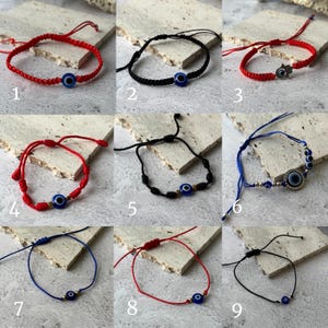 May include: A collection of nine adjustable bracelets, each featuring a blue evil eye charm. The bracelets come in various colors, including red, black, and blue, with different cord designs and embellishments. Some include additional charms.