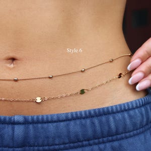May include: A double-strand rose gold waist chain featuring one delicate chain with small beads and a second chain with flat circular discs. The text Style 6 is visible above the chains, which are worn around the midsection over blue pants.