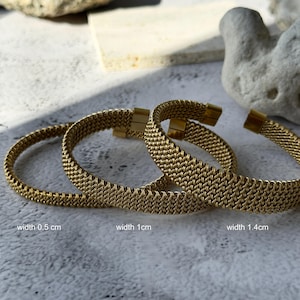 May include: Three gold-colored mesh bracelets with varying widths: 0.5 cm, 1 cm, and 1.4 cm. Each bracelet has a clasp closure. The bracelets are displayed on a light-colored surface.