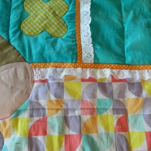 May include: A colorful patchwork quilt with a geometric pattern of circles and semi-circles in shades of pink, yellow, orange, green, and purple. The quilt has a white lace trim and a brown, orange, and white striped border.
