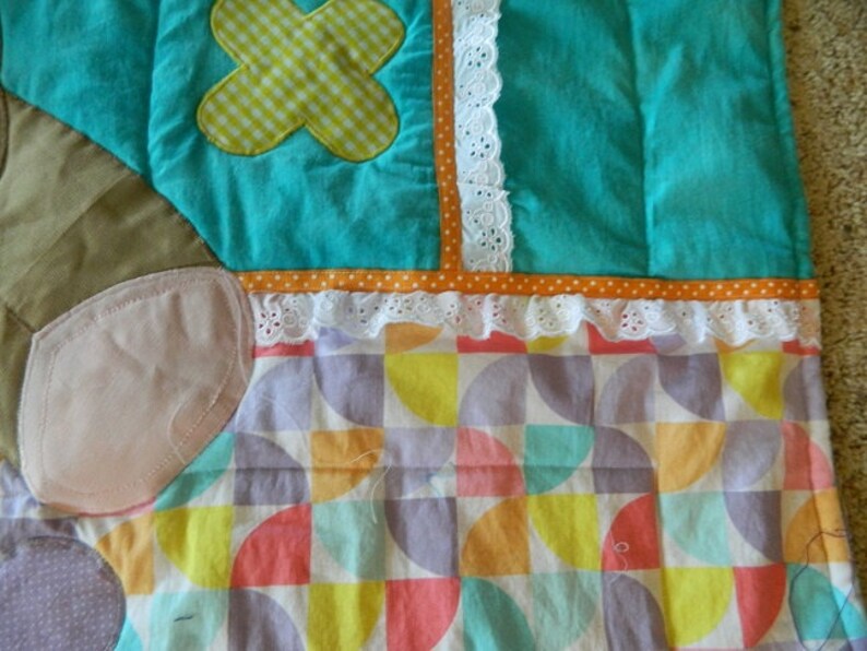May include: A colorful patchwork quilt with a geometric pattern of circles and semi-circles in shades of pink, yellow, orange, green, and purple. The quilt has a white lace trim and a brown, orange, and white striped border.