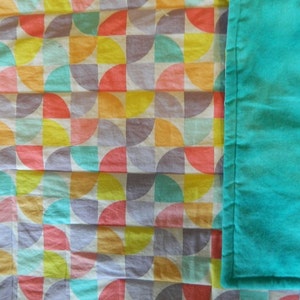 May include: A white fabric with a geometric pattern of colorful semi-circles. The fabric is next to a solid turquoise fabric.