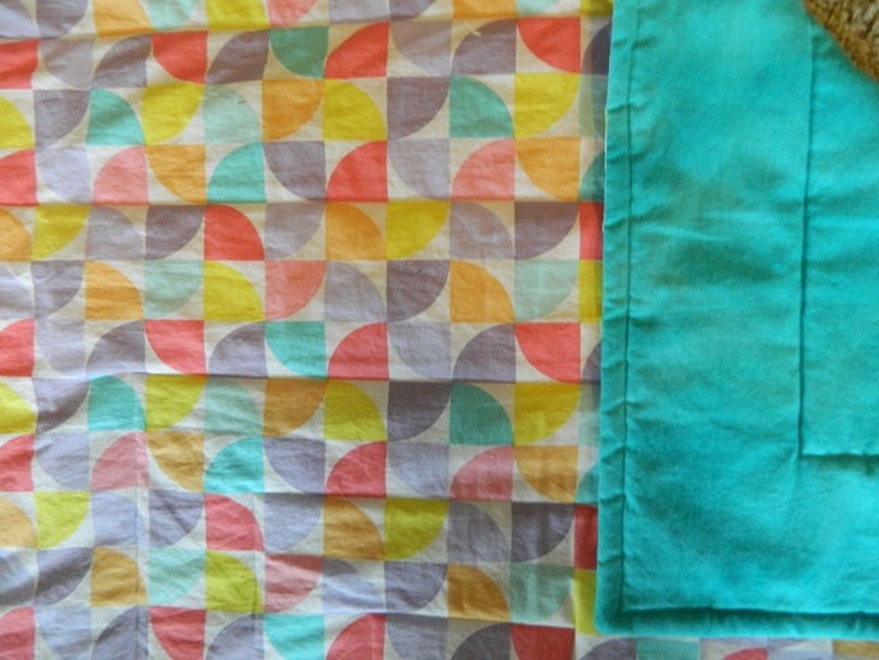 May include: A white fabric with a geometric pattern of colorful semi-circles. The fabric is next to a solid turquoise fabric.