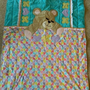 May include: A turquoise and white quilt with a brown teddy bear applique. The quilt has a pattern of colorful half circles.