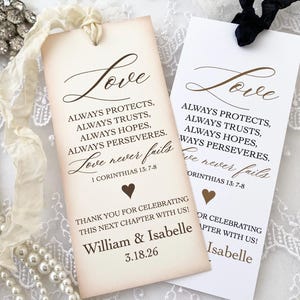 May include: Two cream-colored wedding favor tags with brown text. The text reads "Love always protects, always trusts, always hopes, always perseveres. Love never fails 1 Corinthians 13:7-8". The bottom of the tag says "Thank you for celebrating this next chapter with us! William & Isabelle 3.18.26".