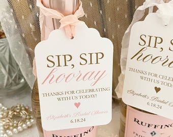 May include: Two white gift tags with pink and gold lettering. The tags read "Sip, Sip Hooray! Thanks for celebrating with us today! Elizabeth's Bridal Shower 6.18.24".