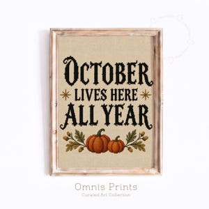 Könnte beinhalten: Ein gerahmtes Kreuzstich-Kunstwerk auf beigem Stoffhintergrund mit dem schwarzen Text "OCTOBER LIVES HERE ALL YEAR", zwei goldenen Sternen und einer Grafik aus zwei orangefarbenen Kürbissen, umgeben von grünen Blättern und kleinen braunen Eicheln.