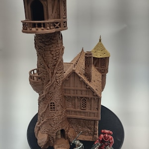 May include: A brown and tan miniature tower with a stone and wood exterior. The tower has a small door and windows. There are two miniature figures standing in front of the tower.