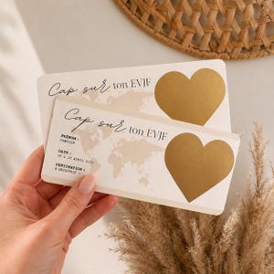 May include: Two ivory-colored cards with gold heart-shaped accents. The cards have the text "Cap sur ton EVJF" and include a world map design. The bottom card has the name "Camille" and the date "19 & 20 AVRIL 2025".