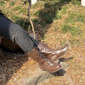 May include: A pair of brown leather lace-up boots with a tall shaft. The boots are worn and have a distressed look.
