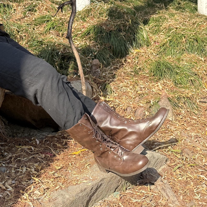 May include: A pair of brown leather lace-up boots with a tall shaft. The boots are worn and have a distressed look.