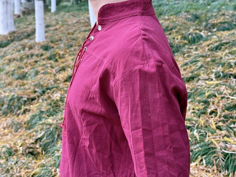May include: A burgundy long-sleeved shirt with a lace-up neckline and a high collar.