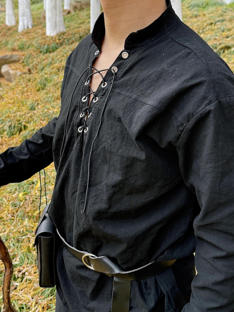 May include: A black long-sleeved shirt with a lace-up neckline and silver eyelets. The shirt has a relaxed fit and is worn with a black leather belt.