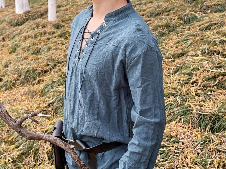 May include: A blue long-sleeved shirt with a lace-up neckline and a brown leather belt. The shirt is made of a soft, lightweight fabric and has a relaxed fit.