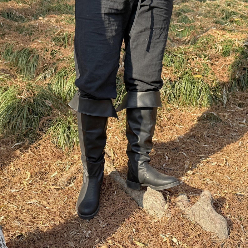 May include: A pair of black leather knee-high boots with a fold-over top. The boots are worn with black pants.