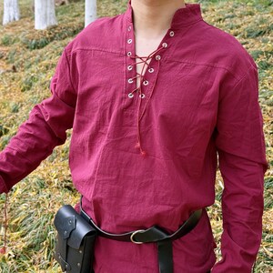 May include: A burgundy long-sleeved shirt with a lace-up neckline and a black leather belt. The shirt has a relaxed fit and is made of a soft, comfortable fabric.