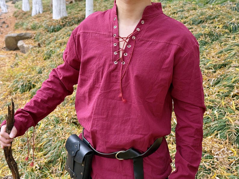 May include: A burgundy long-sleeved shirt with a lace-up neckline and a black leather belt. The shirt has a relaxed fit and is made of a soft, comfortable fabric.