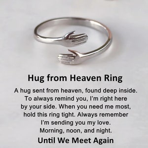 Può includere: Anello d'argento con due mani intrecciate, che formano un abbraccio. L'anello è inciso con le parole "Hug from Heaven Ring" e una poesia che spiega il suo significato.