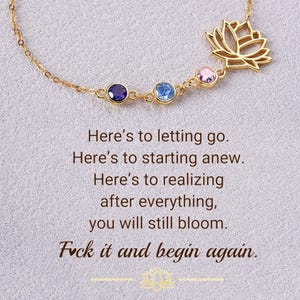 May include: A gold-colored necklace with a lotus flower pendant and three colorful gemstones. The necklace has the text "Here's to letting go. Here's to starting anew. Here's to realizing after everything, you will still bloom. Fuck it and begin again."