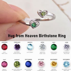 May include: A silver-colored ring with two heart-shaped settings, each holding a gemstone. The ring is labeled "Hug from Heaven Birthstone Ring." Below are birthstone options with associated months and meanings.