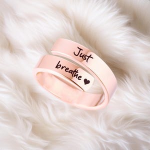 May include: A rose gold-colored ring with the words "Just breathe" and a small heart engraved on it.